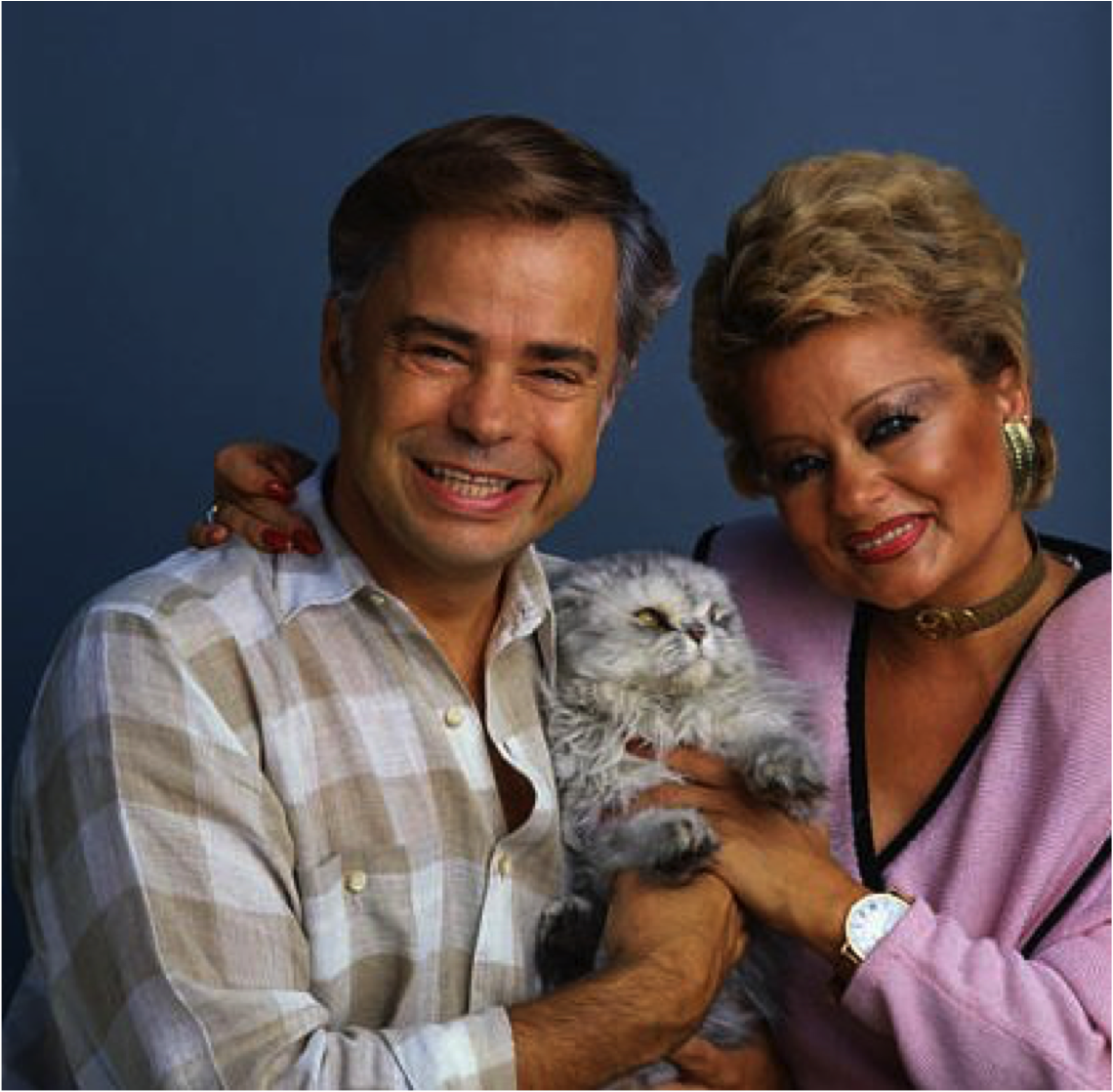 Smiling man and woman holding a gray, long-haired cat between them