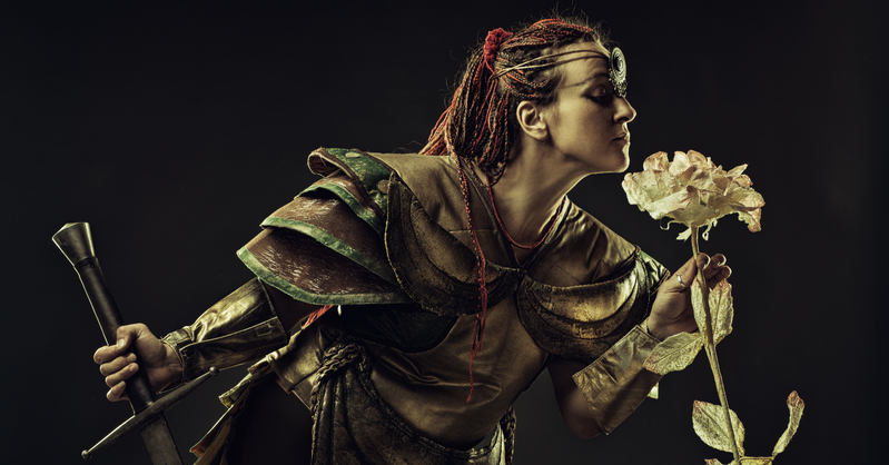 Graceful, female warrior holding a sword in one hand and a beautiful flower in the other as she bends to smell its fragrance.